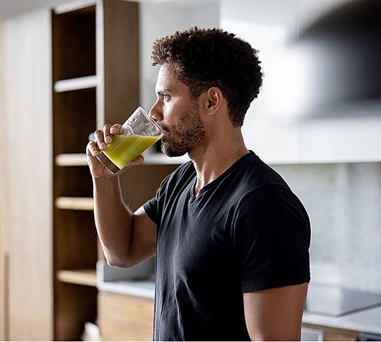 Man drinking green juice in modern kitchen.